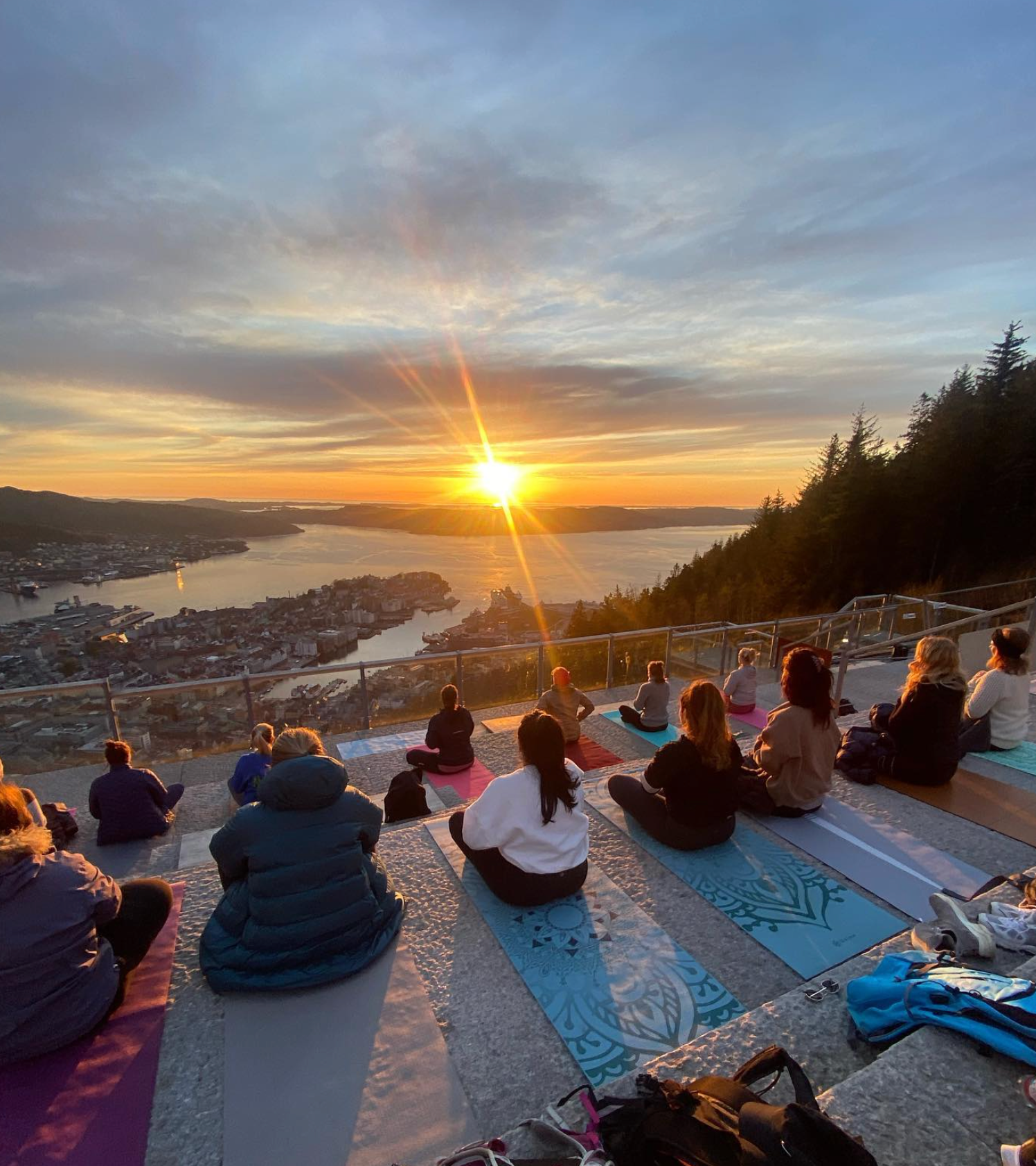 Mennesker som gjør fjell yoga i solnedgang med utsikt over Bergen