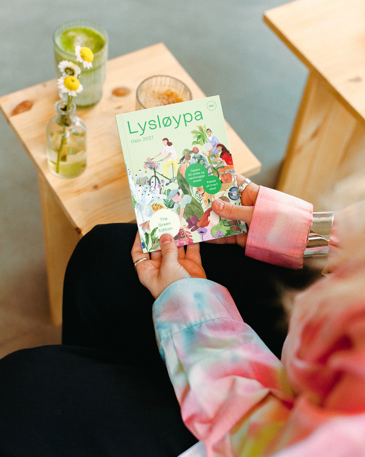 Lysløypa Oslo 2027 – The Green Edition, holdt i hendene ved et bord med kaffe og blomster